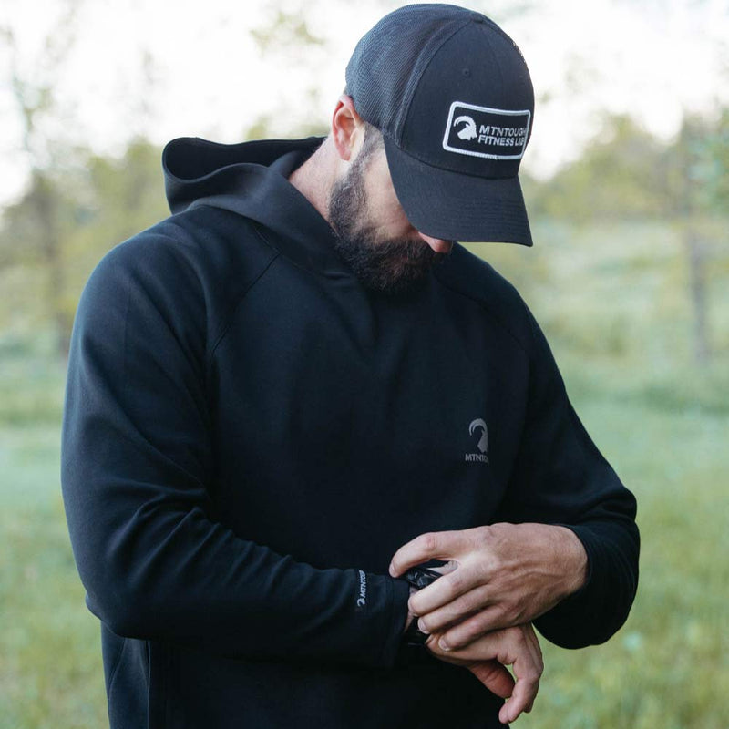 Man wearing a black hoodie and cap with a logo, standing outdoors.